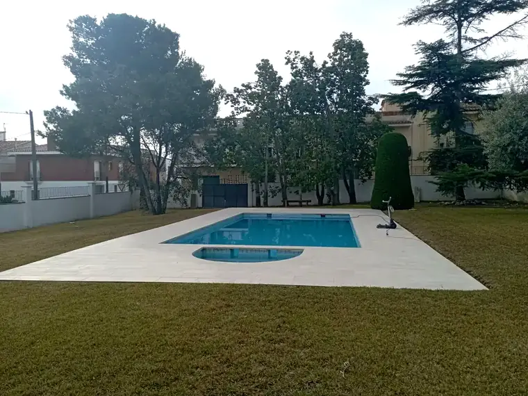 Piscina rectangular con escalera de obra en semicírculo, rodeada de césped, con un robot limpiafondos junto al borde
