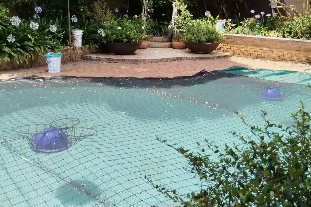 Piscina de jardín tapada con una red que cubre el agua hasta el borde