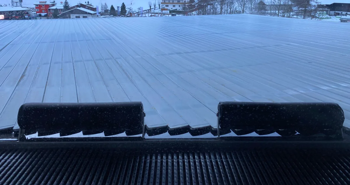Cubierta automática de lamas cerrada sobre una piscina exterior en invierno, con el banco del enrollador en primer plano y nieve al fondo