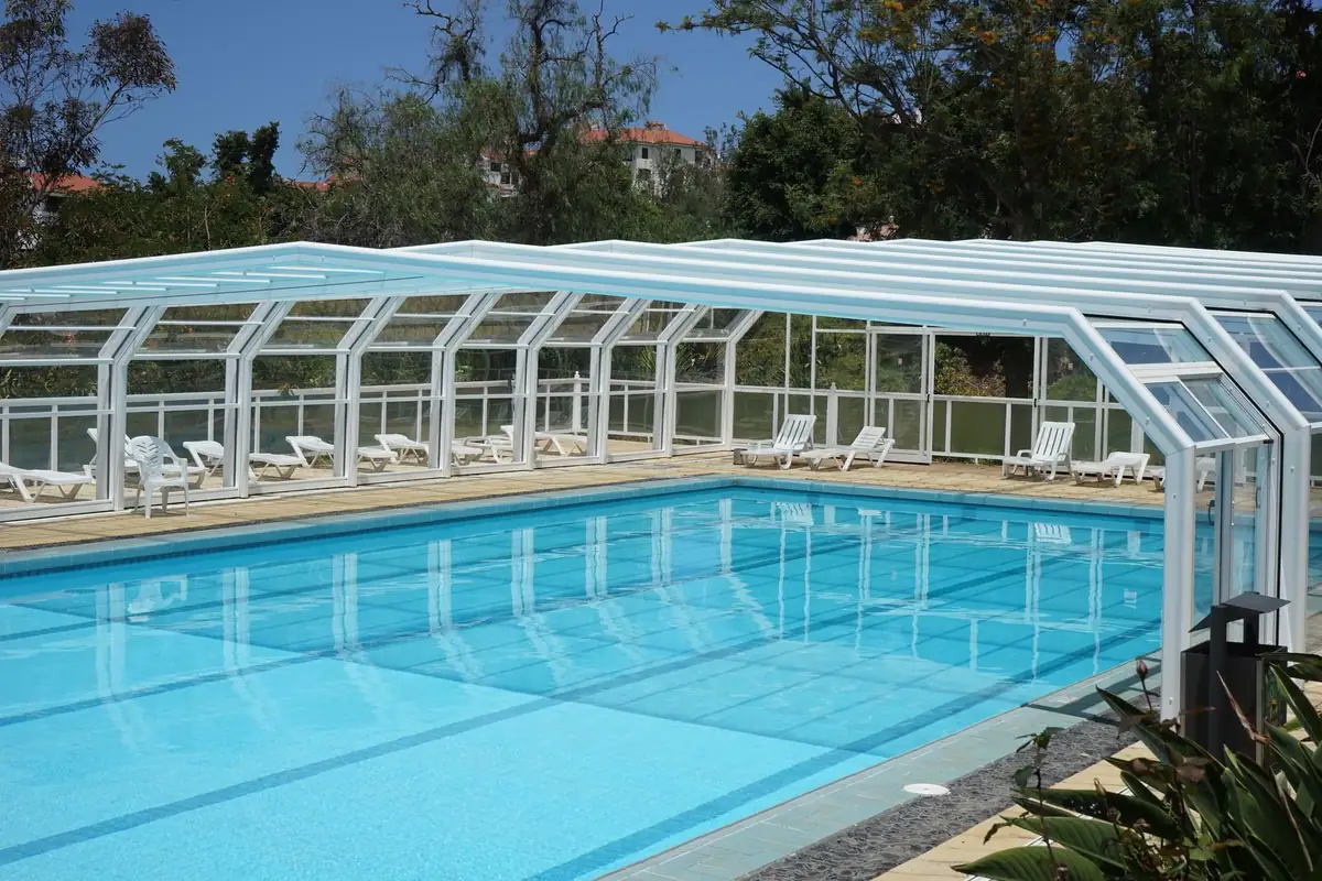 Cubierta telescópica alta de aluminio blanco y paneles transparentes recogida en parte sobre una piscina exterior