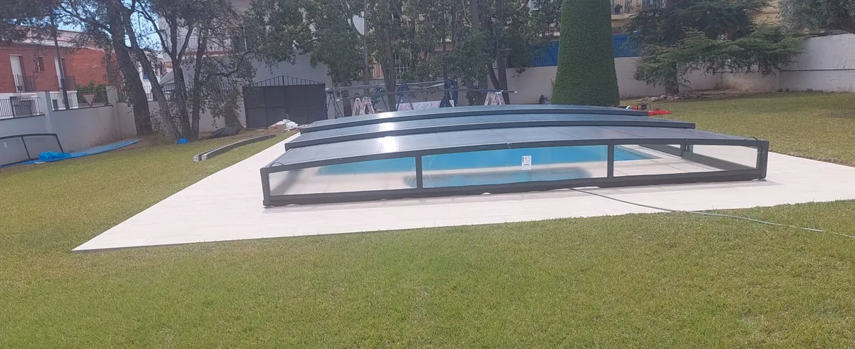 Piscina de jardín con varios módulos de una cubierta telescópica baja colocados sobre el vaso y caballetes al fondo