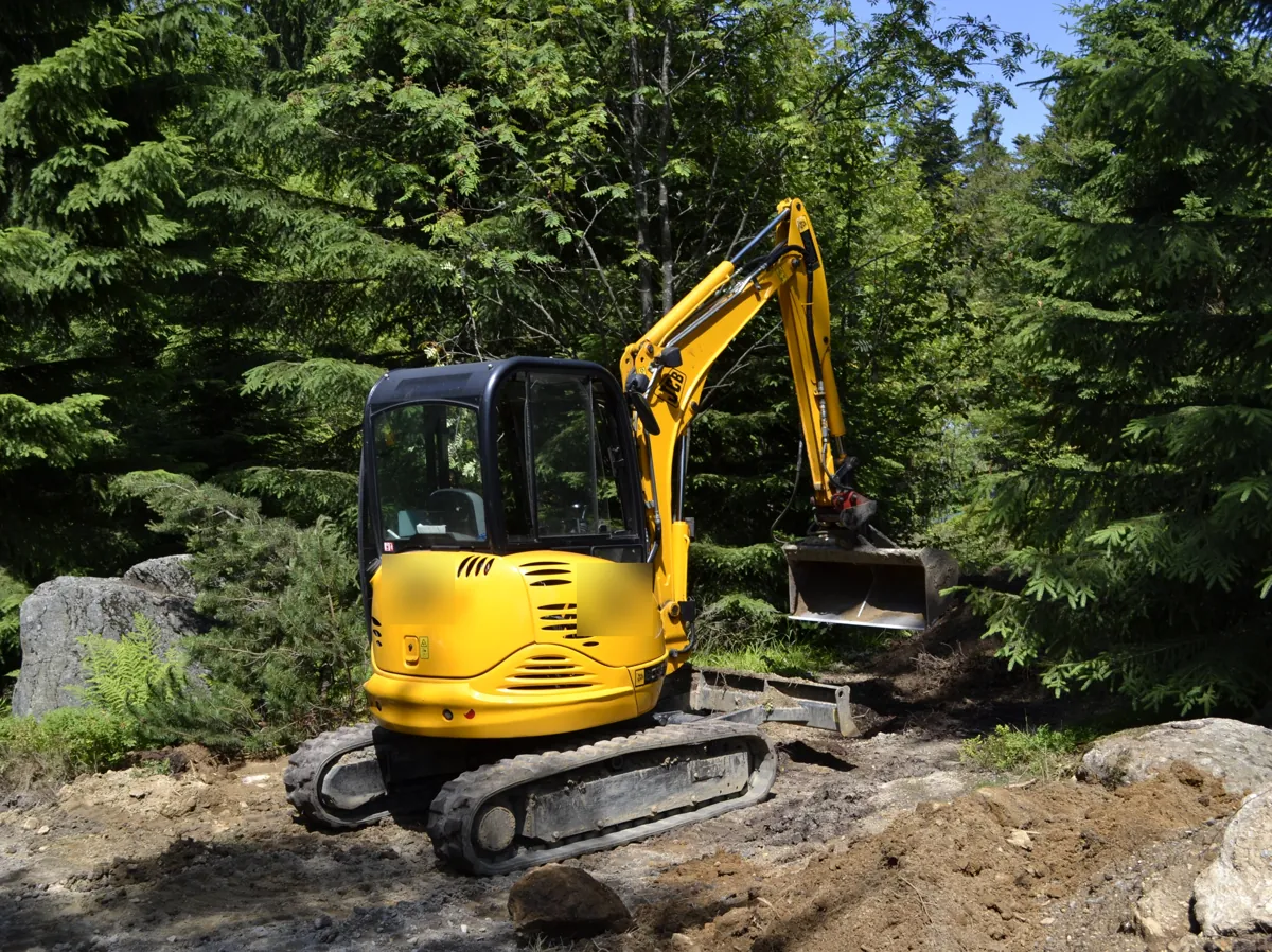 Miniexcavadora amarilla abriendo terreno entre árboles, el tipo de movimiento de tierras que suele pedir licencia