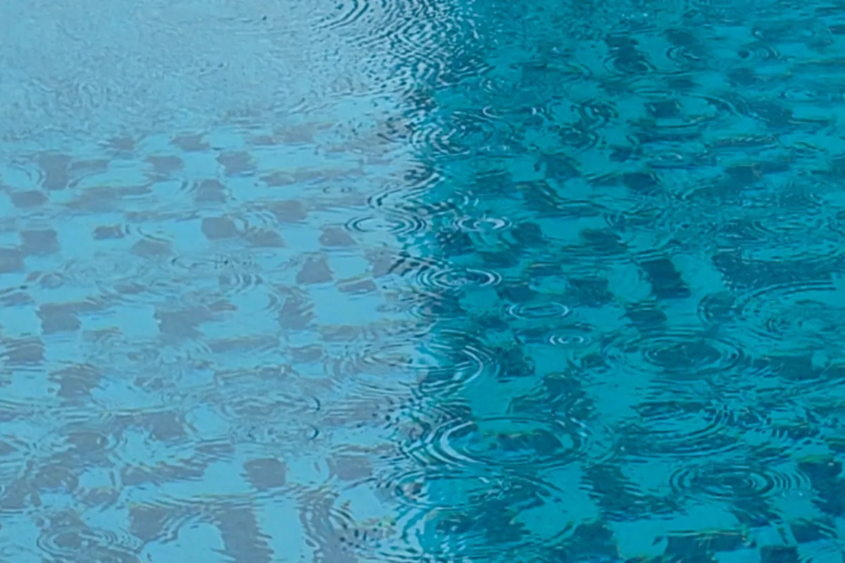 Gotas de lluvia formando ondas en el agua de una piscina con gresite azul