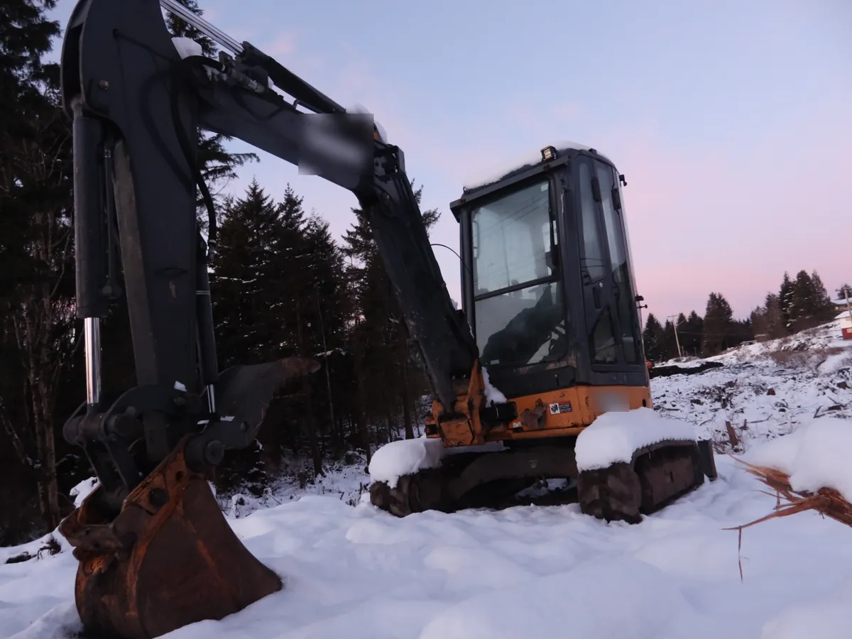 Miniexcavadora parada en una obra cubierta de nieve al amanecer