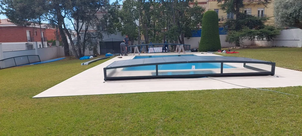 Montaje de una cubierta telescópica baja: un módulo ya colocado sobre la piscina y perfiles sobre el césped