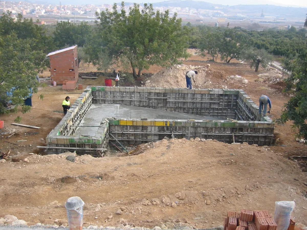 Obra de una piscina particular en una parcela con árboles: vaso de hormigón con el encofrado de las paredes montado y tierra de la excavación alrededor