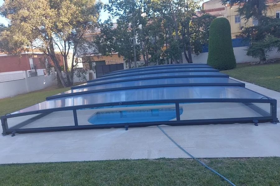 La misma piscina con una cubierta telescópica baja de aluminio y policarbonato cerrada, a la luz del atardecer