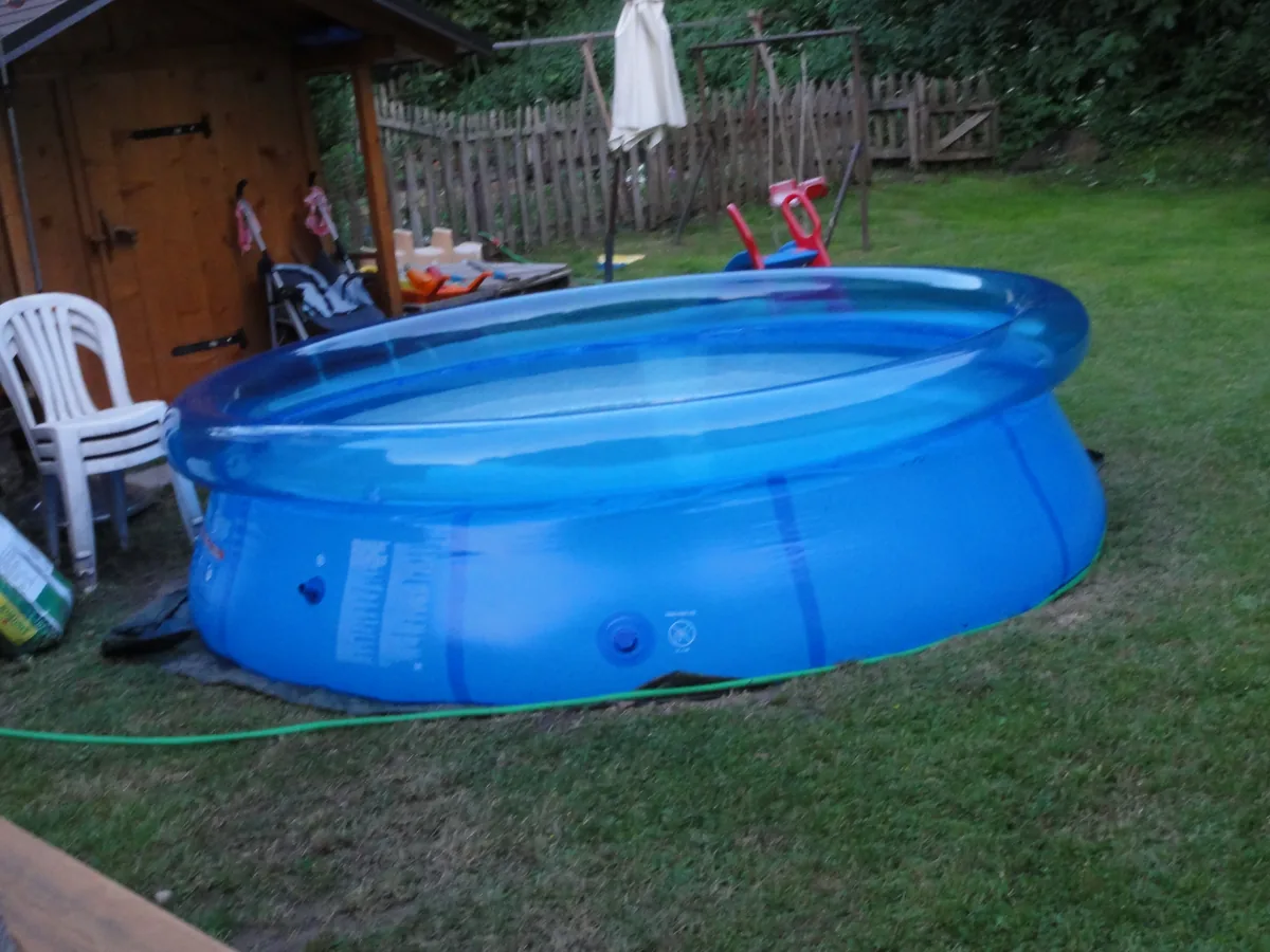Piscina hinchable azul montada en el césped de un jardín junto a una caseta de madera