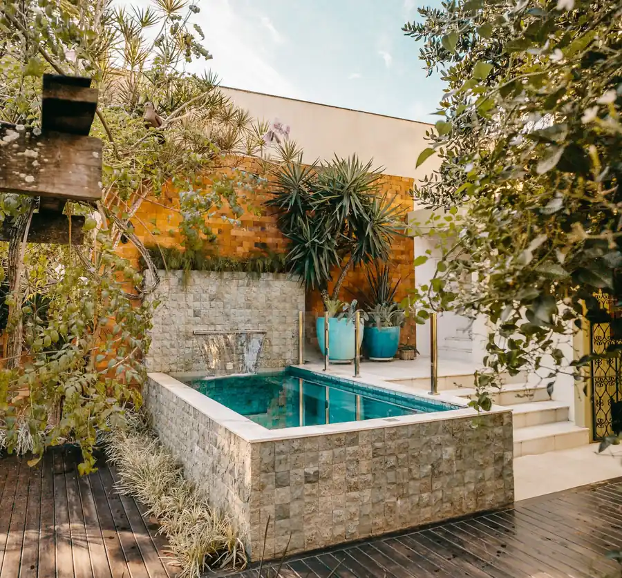 Pequeña piscina elevada de obra revestida de piedra en un patio con tarima de madera y plantas