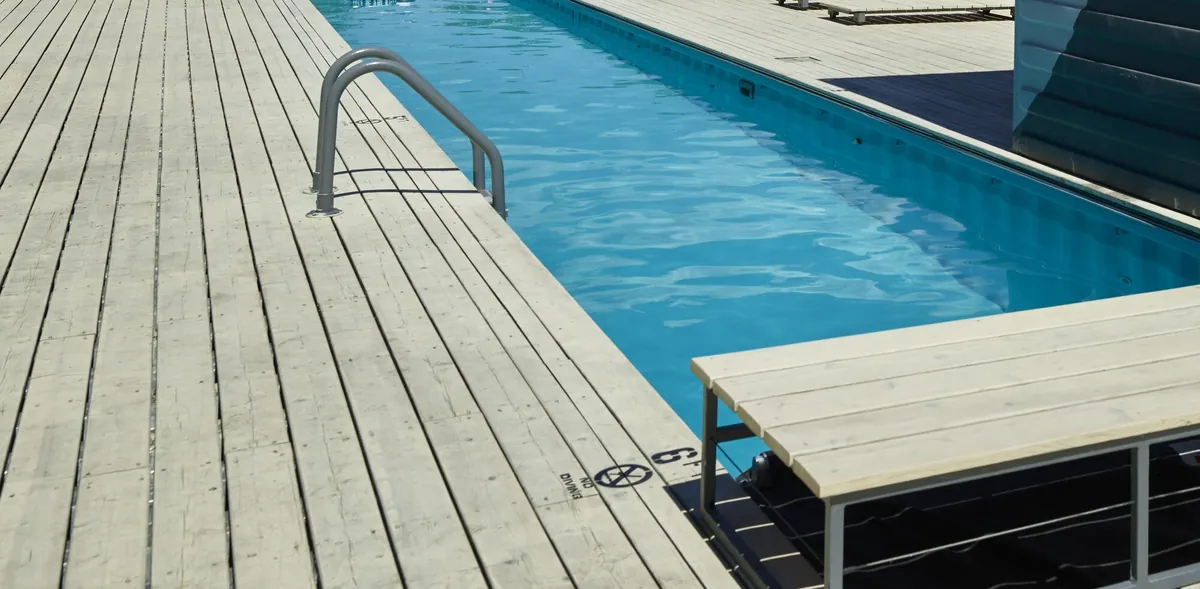 Piscina estrecha y alargada con escalera de acero, junto a una tarima de madera y un módulo de servicio hecho con un contenedor marítimo