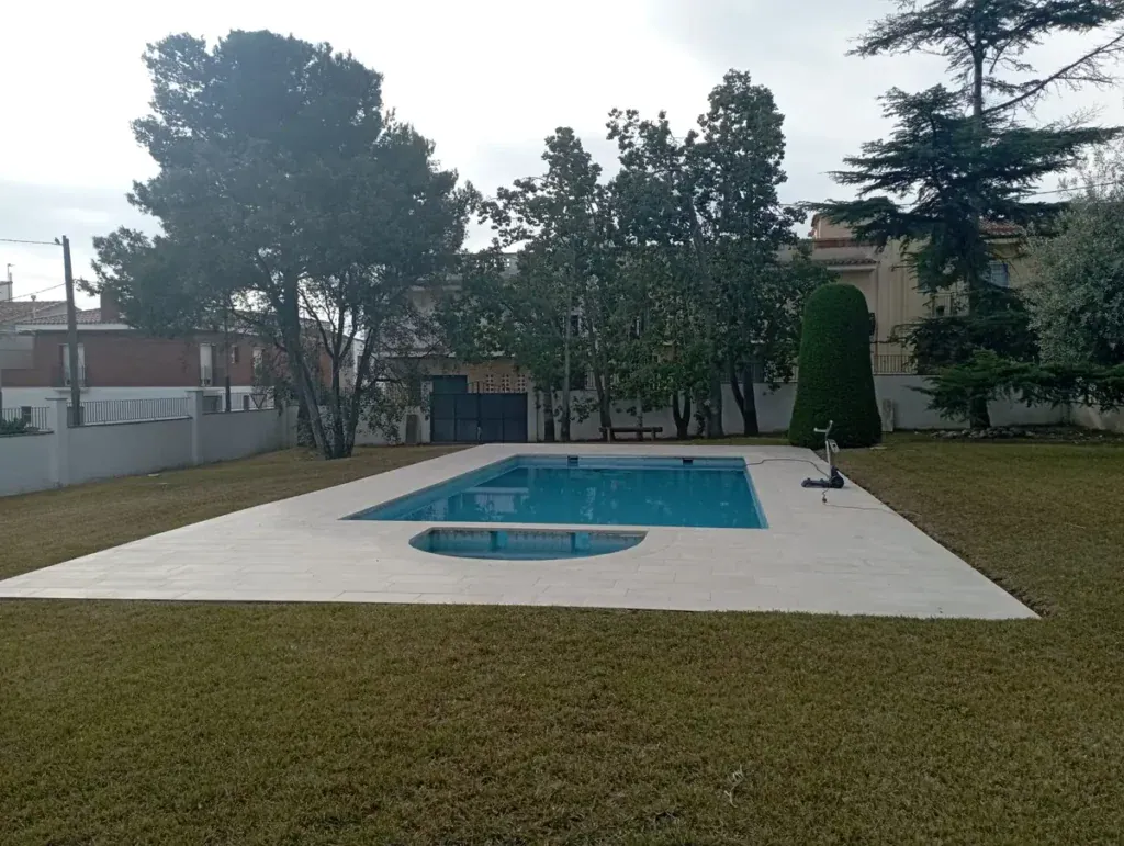 Piscina familiar rectangular con agua limpia, playa de piedra clara y jardín de césped