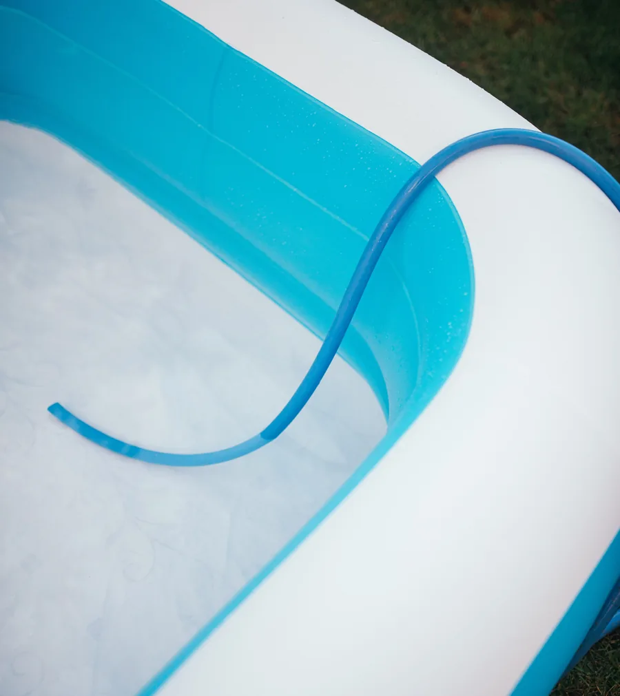 Piscina hinchable blanca y azul con una manguera azul apoyada en el borde para llenarla