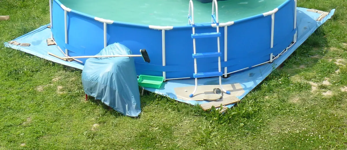 Piscina tubular desmontable azul montada sobre una lona en el césped, con su escalera