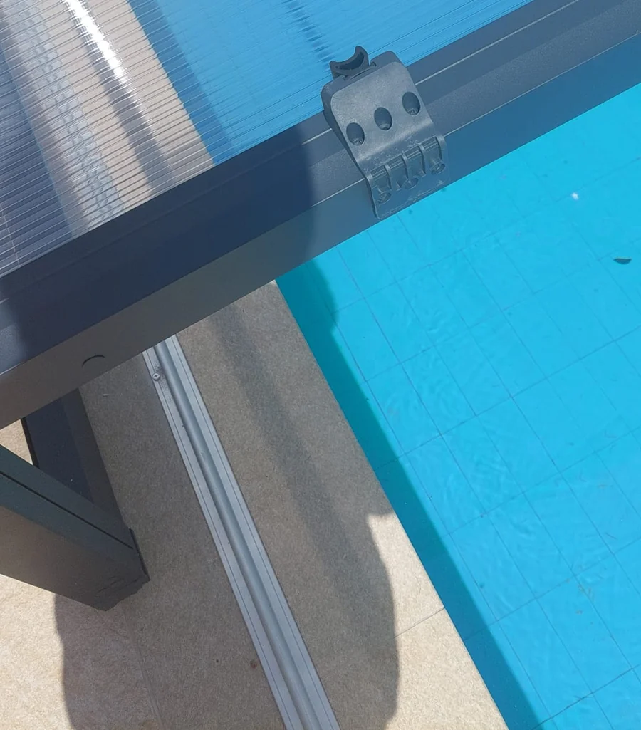 Detalle del perfil de aluminio con policarbonato celular, la pieza de bloqueo y el raíl de aluminio sobre la playa, con el gresite azul bajo el agua
