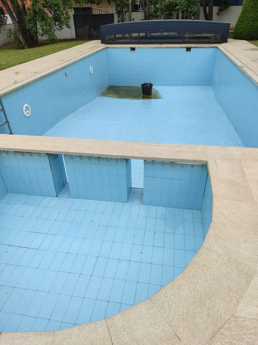 Piscina vaciada con gresite azul claro, juntas oscurecidas bajo la coronación y restos de lodo en la zona honda
