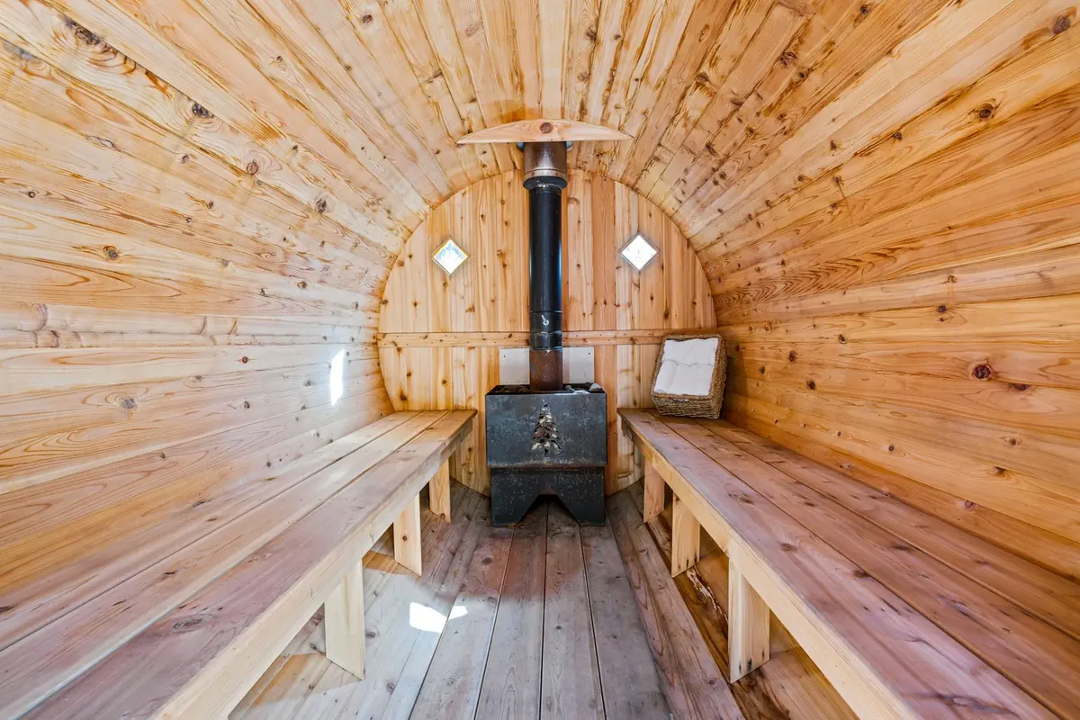 Interior de una sauna de barril con bancos de madera a los lados y estufa de leña al fondo