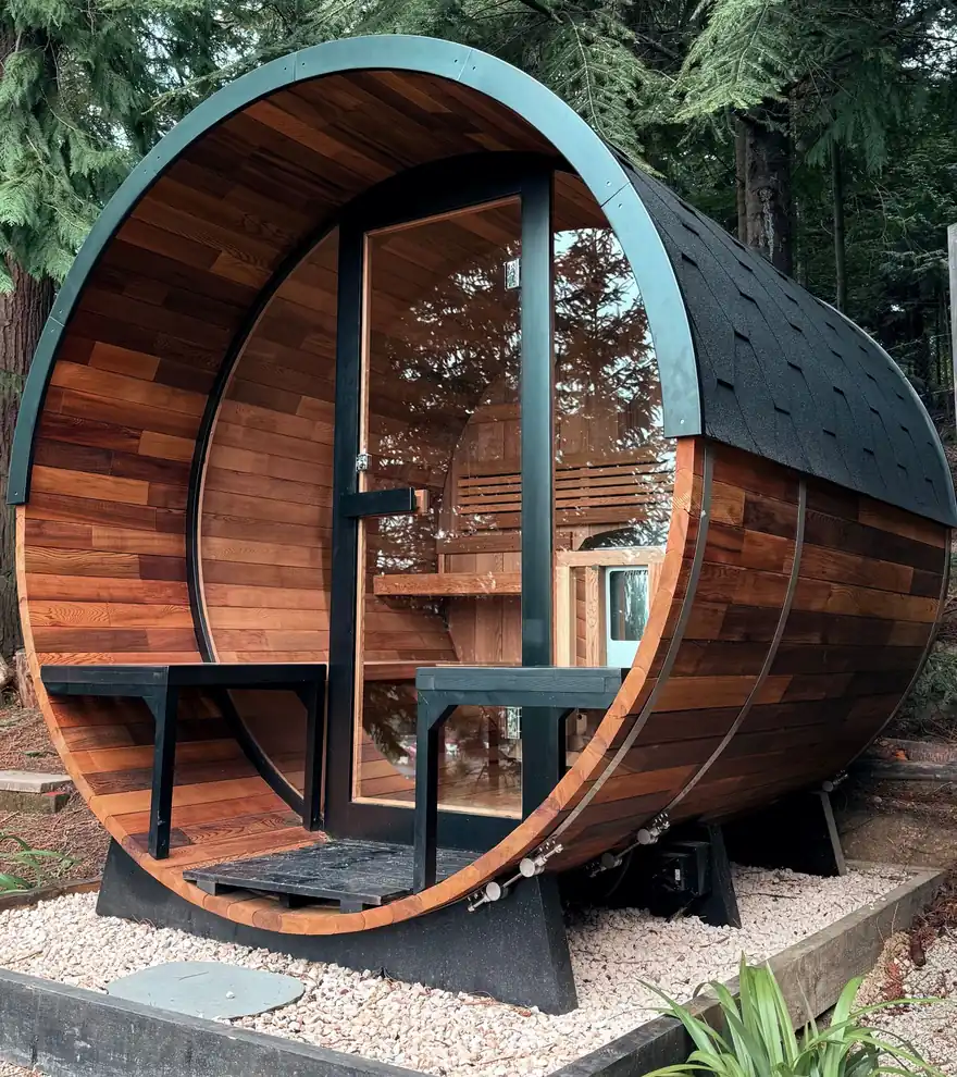 Sauna de exterior de barril con frontal de cristal sobre una base de grava en un jardín