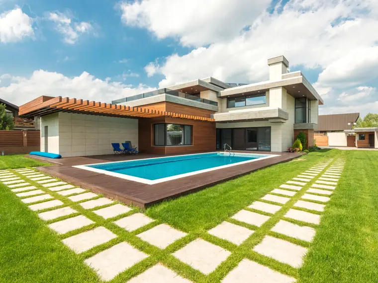 Piscina rectangular con borde claro en un jardín de césped junto a una casa